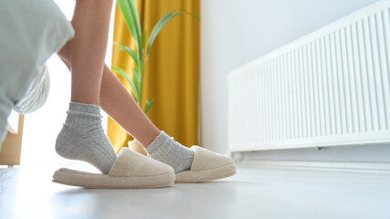 Children's feet in warm socks and slippers. Early in the morning a young girl puts on slippers after sleeping. Comfort and relaxation in the cold season concept. Heater radiator on background.