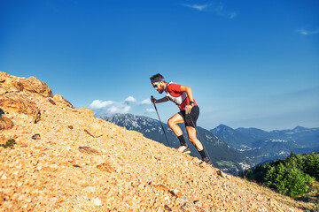 Young man uphill on rocky slope pushes with poles