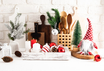 Front view of eco-friendly wooden kitchen utensils and Christmas decorations in a wooden box on a white wooden table against a brick wall.