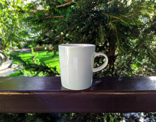 white cup along with coffee on the railing of the house and garden background.