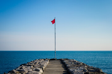 La bandiera rossa che indica il divieto di balneazione issata su un palo alla fine di un...