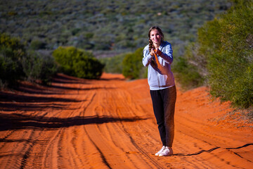 Fototapeta na wymiar A beautiful long-haired girl plays with red sand on a sandy road in the desert in the middle of nowhere; francois peron national park in western australia, terra rosa