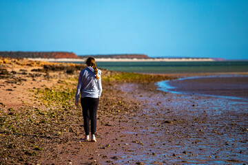 girl walks on red sand beach with red cliffs in the background, terra rosa in australia, holidays in western australia, francois peron national park