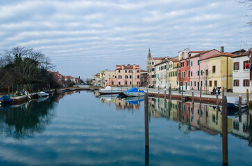 Fototapeta na wymiar Un canale del piccolo borgo di Malamocco al Lido di Venezia in una giornata nuvolosa d'inverno con le barche ormeggiate