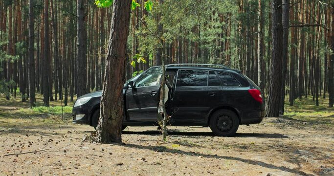 Black small car in the middle of beautiful forest. Delighted young blonde daughter with mother arrivinf on woods for hikking treking relaxing doing axercises yoga camping at weekends.