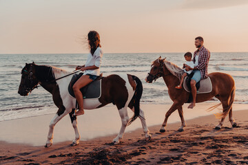 The family spends time with their children while riding horses together on a sandy beach. Selective focus 