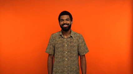 cheerful african american man with beard standing in shirt on orange background.