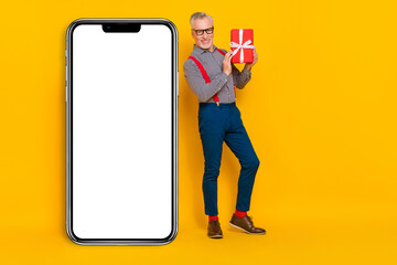 Full length body size view of attractive grey-haired man holding giftbox copy space isolated over bright yellow color background