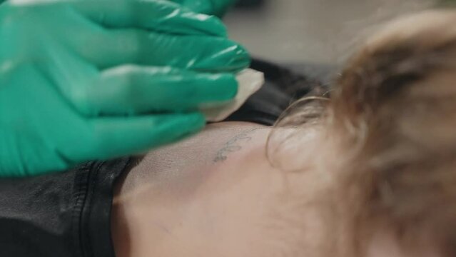 In neck of client master makes tattoo with inscription using tattoo machine.
