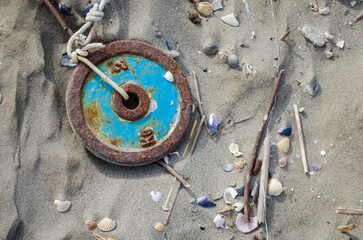 Una ruota metallica blu arrugginita e legata da una corda sulla sabbia della spiaggia di...