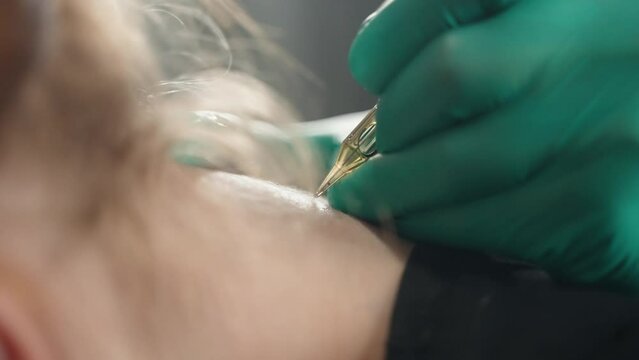 Close-up side view of client's neck, master makes tattoo with tattoo machine.