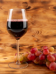 Glass of wine and grapes on a wooden background.
