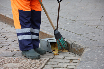 Worker in uniform with a broom clean the sidewalk, collects fallen leaves in a dustpan. Street...
