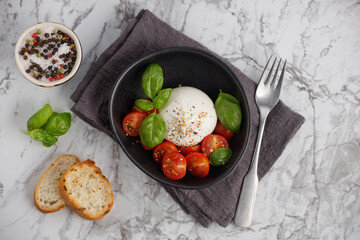 Fresh Italian burrata with tomatoes and basil on a plate on a marble table, top view. Cheese ball burrata from mozzarella and cream. Healthy food