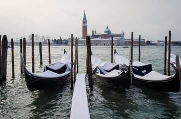 Fototapeta na wymiar Le gondole ormeggiate nel bacino di San Marco a Venezia, coperte dalla neve in una giornata invernale