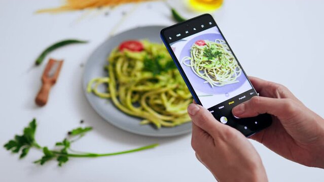 Shooting cooked food pasta pasta on smartphone smartphone for social media, Blogger taking pictures of pasta pasta with green sauce cooked for vegetarians on mobile phone
