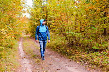 Obraz premium A middle age male hiking with a backpack.Man walks along the autumn forest path way.A healthy lifestyle in nature.