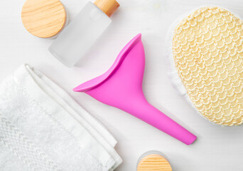 Fototapeta na wymiar Device for women, pee funnel, tool that helps urinating standing. Pink silicone funnel between hygiene products. Flat lay view, studio shot.