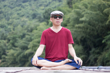 Fototapeta premium The man relaxed man in a crimson t-shirt enjoying nature breathing fresh air meditating on the river on a vacation day. 