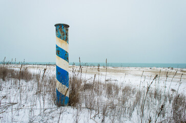 Un palo colorato in bianco e blu sulla spiaggia del Lido di Venezia coperta dalla neve in una...