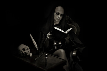 An emotional woman dressed for Halloween as a nun sits on a black background in an armchair with a notebook with a pen.
