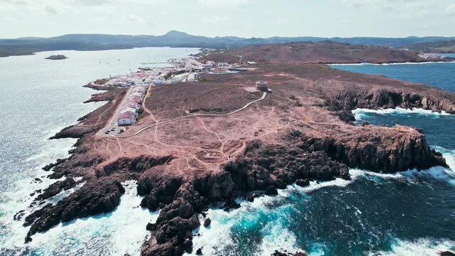 View from above of Fornells village located in a bay in the north of the Menorca 
Drone view of a harbour filled with llauts, the traditional Menorcan fishing craft, surrounded by white washed houses.