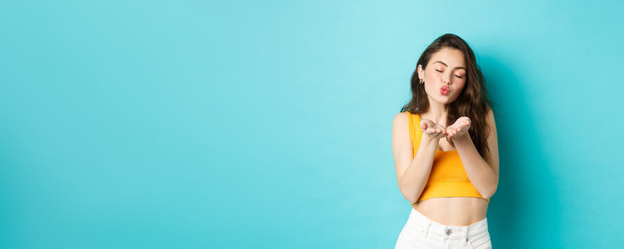 Romantic Silly Woman Close Eyes And Pucker Lips, Blowing Air Kiss At You, Standing Dreamy Against Blue Background