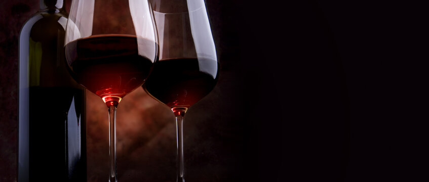 a bottle of red wine and two wine glasses on a dark background. Cozy winter evening background with copy space