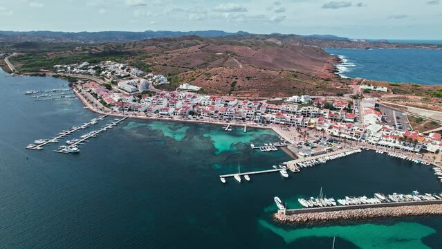 View from above of Fornells village located in a bay in the north of the Menorca 
Drone view of a harbour filled with llauts, the traditional Menorcan fishing craft, surrounded by white washed houses.