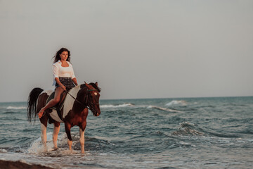 Woman in summer clothes enjoys riding a horse on a beautiful sandy beach at sunset. Selective focus 