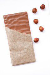 Chocolate bar with hazelnuts in opened pack on white table background. Closeup