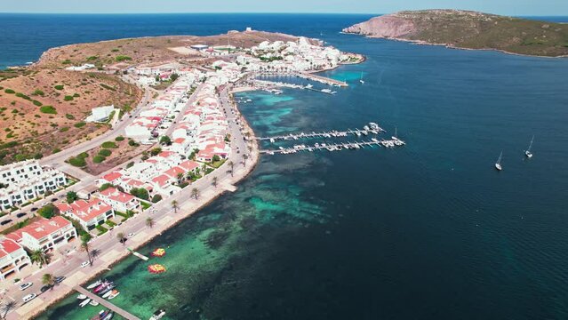 View from above of Fornells village located in a bay in the north of the Menorca 
Drone view of a harbour filled with llauts, the traditional Menorcan fishing craft, surrounded by white washed houses.