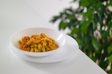 Italian pasta with shrimp and turmeric on a white table in a white plate
