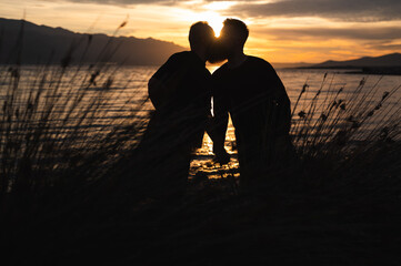 Silhouette of gay couple kissing in sunrise,  enjoying early morning beautiful sun reflecting on...