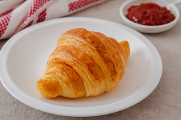 Fresh croissant on white plate and jam on table.