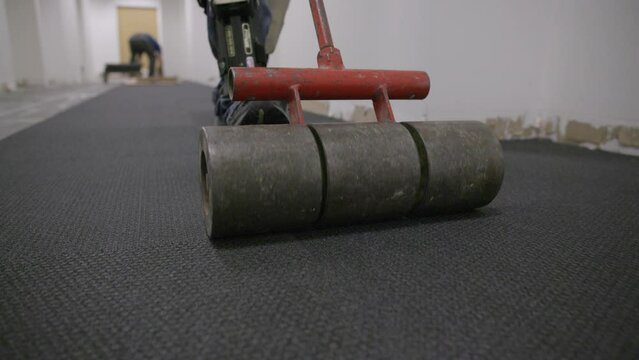 Slow motion following a metal roller that is rolling along squares of carpet.