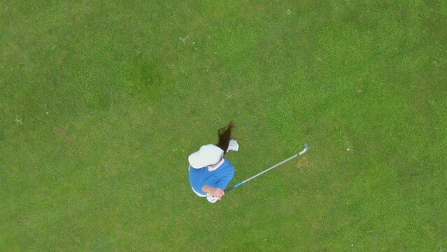 OVERHEAD AERIAL Drone shot of Caucasian female playing golf, striking a ball during the course