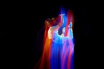 In miracle flight. Young sportive dancer in white clothes levitating, moving over dark background in mixed neon light. Creative art, aspiration, music, fashion, dance