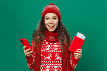 Traveler woman in cozy sweater hat hold passport ticket use mobile phone isolated on plain dark green background Tourist travel abroad in free spare time rest getaway Air flight trip journey concept