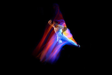 Dance in motion. Studio shot of flying, jumping dancer or gymnast performing tricks in the air over black background with mixed neon glowing rays