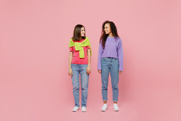 Full body young two friends cheerful happy fun cool positive women 20s wears green purple shirts together stand look to each other isolated on pastel plain light pink color background studio portrait.