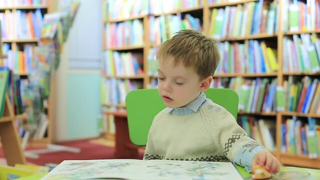 The kid carefully examines the pictures in fairy-tale books while sitting in the children's library. Blurred background