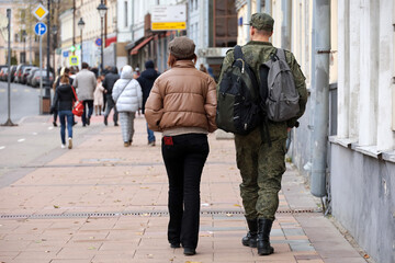 Girl with soldier of military forces in camouflage walking down the city street in autumn