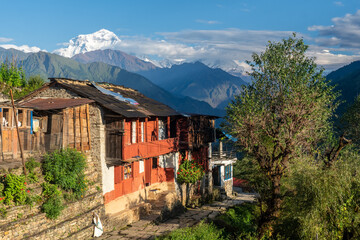 Een hoge besneeuwde berg die uittorent boven een dorp met houten huizen en leien daken en geplaveide paden, Dhaulagiri, & 39 s werelds 7e hoogste, 8.167 meter, Shikha, Nepal, Annapurna Circuit