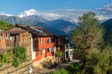 Fotobehang Dhaulagiri Een hoge besneeuwde berg die uittorent boven een dorp met houten huizen en leien daken en geplaveide paden, Dhaulagiri, & 39 s werelds 7e hoogste, 8.167 meter, Shikha, Nepal, Annapurna Circuit