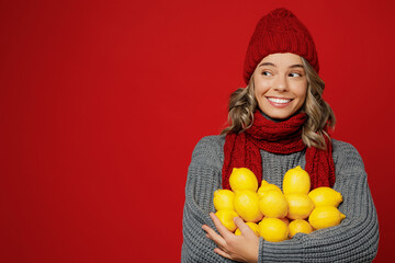 Young woman in grey sweater scarf hat hold in hands bunch of lemons fruit look aside isolated on...