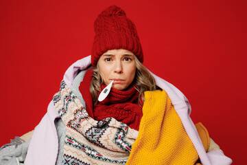 Young frozen woman wear scarf hat wrapped in many plaids hold thermometer in mouth isolated on...