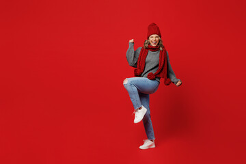 Full body young woman wear grey sweater scarf hat do winner gesture celebrate clenching fists say yes isolated on plain red background Healthy lifestyle ill sick disease treatment cold season concept