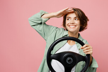 Young smiling happy cool woman 20s she wear green shirt white t-shirt hold steering wheel driving...
