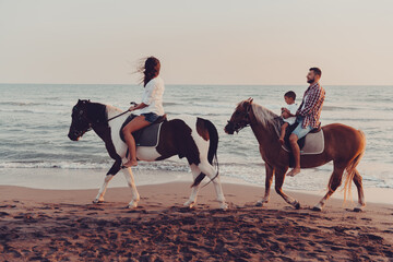The family spends time with their children while riding horses together on a sandy beach. Selective...